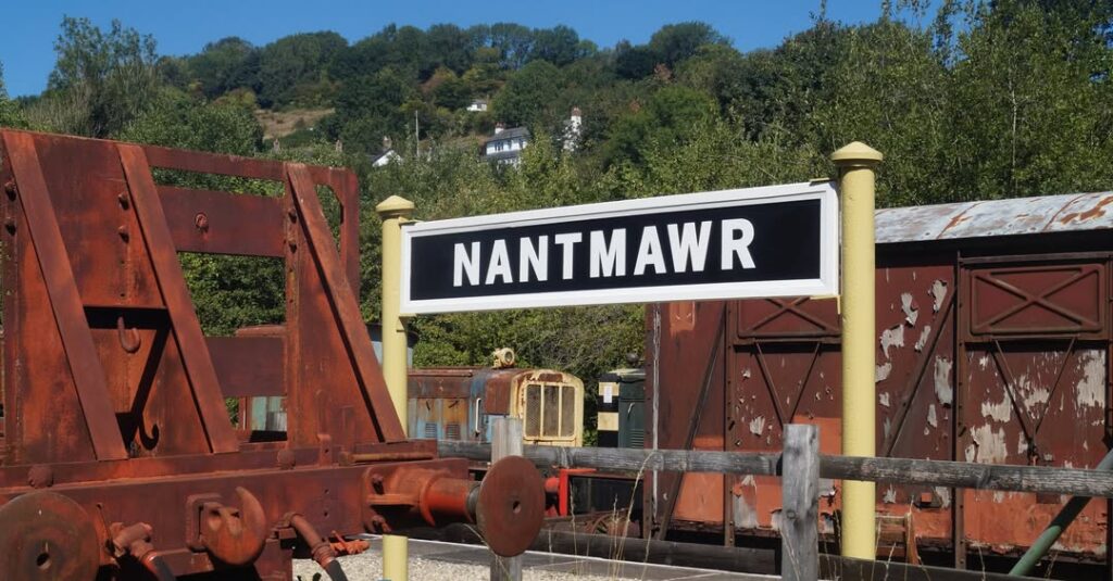 Photo of platform sign at Nantmawr with various bits of rolling stock visible nearby.