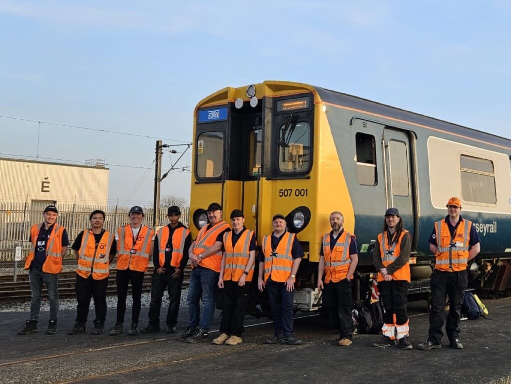Class 507 Preservation Society volunteers pose in front of 507001 in Litchurch Lane works, Derby